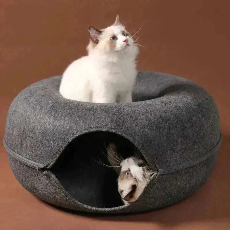 Gray donut-shaped cat tunnel bed with two cats, one sitting on top and one inside the cozy wool felt bed